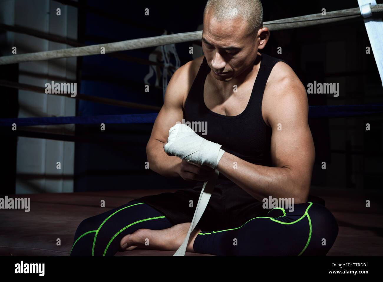 Uomo maturo bendaggio di incarto a portata di mano mentre seduto contro il pugilato ring in palestra Foto Stock