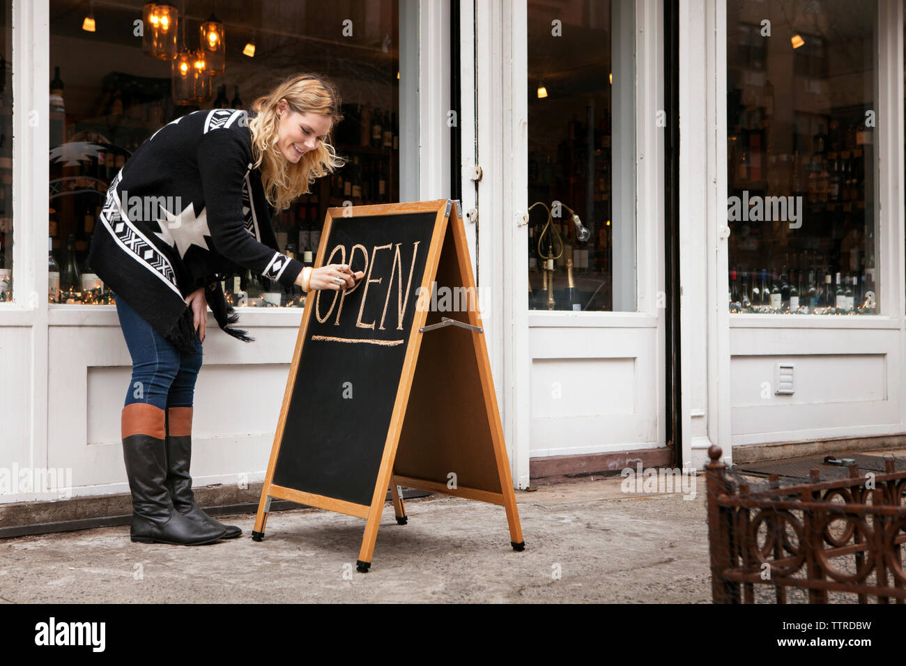 Femmina proprietario di piccola impresa facendo segno di apertura al di fuori del negozio del vino Foto Stock