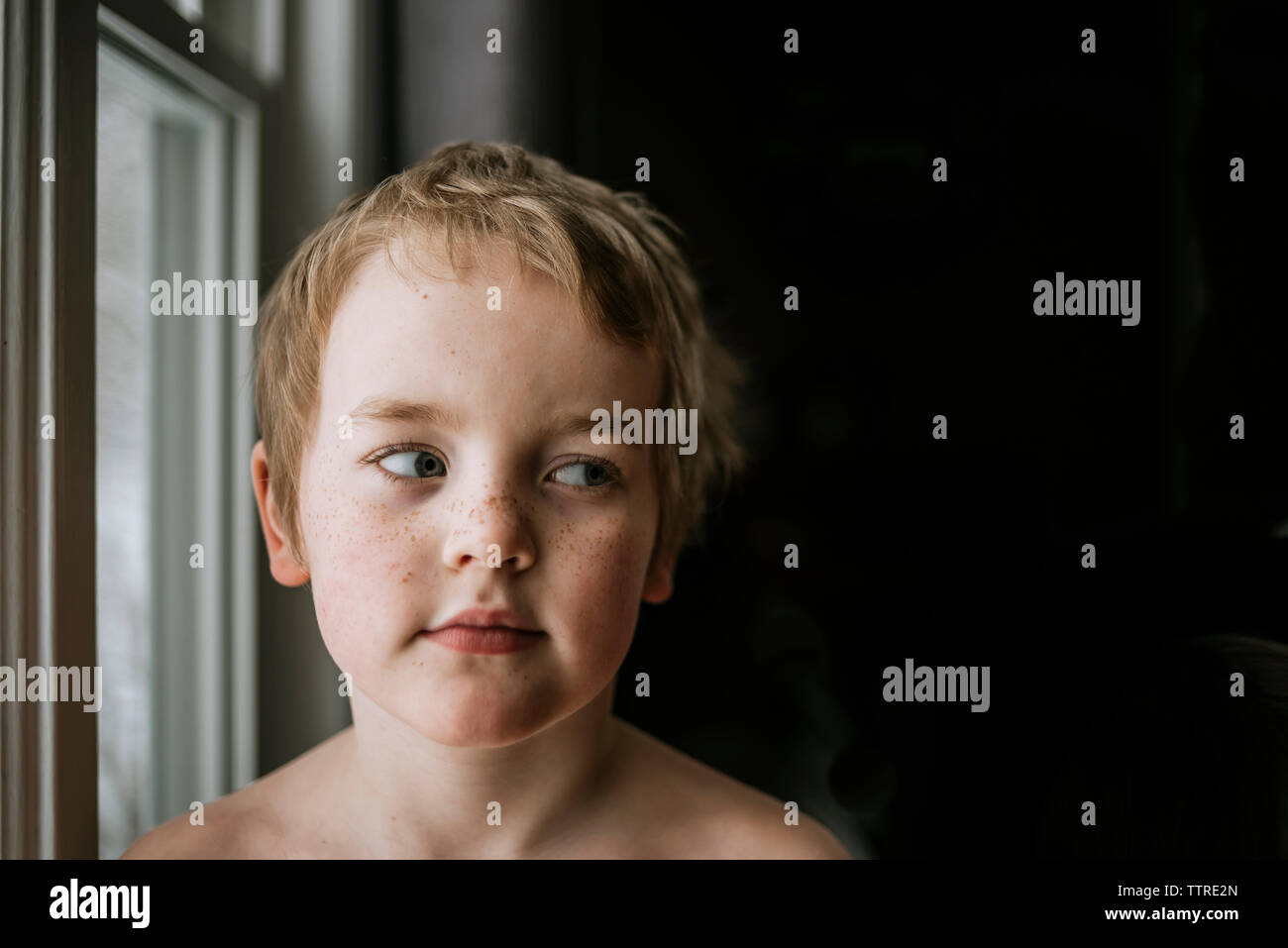 Close-up di ragazzo cerca attraverso lateralmente sguardo in camera oscura Foto Stock