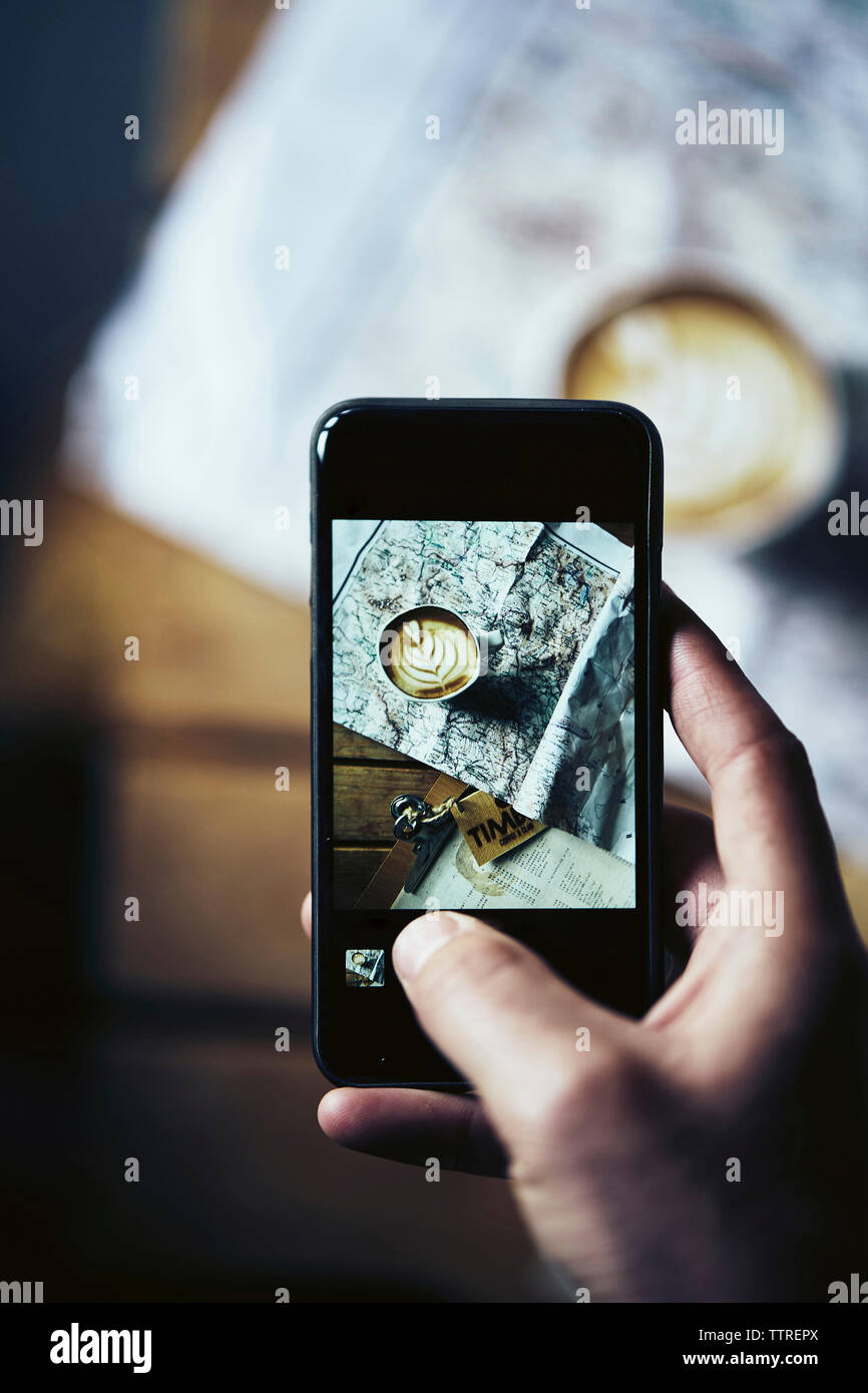 Ritagliate la mano dell'uomo fotografare la tazza di caffè con la mappa sul tavolo con telefono cellulare a casa Foto Stock