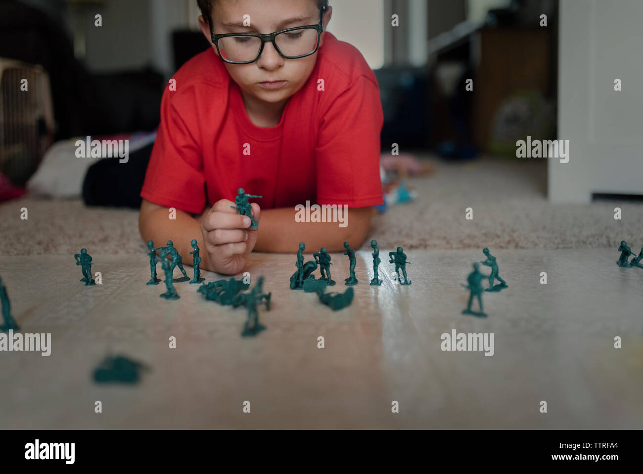 Ragazzo giocando con plastica in miniatura toy soldiers sul pavimento a casa Foto Stock