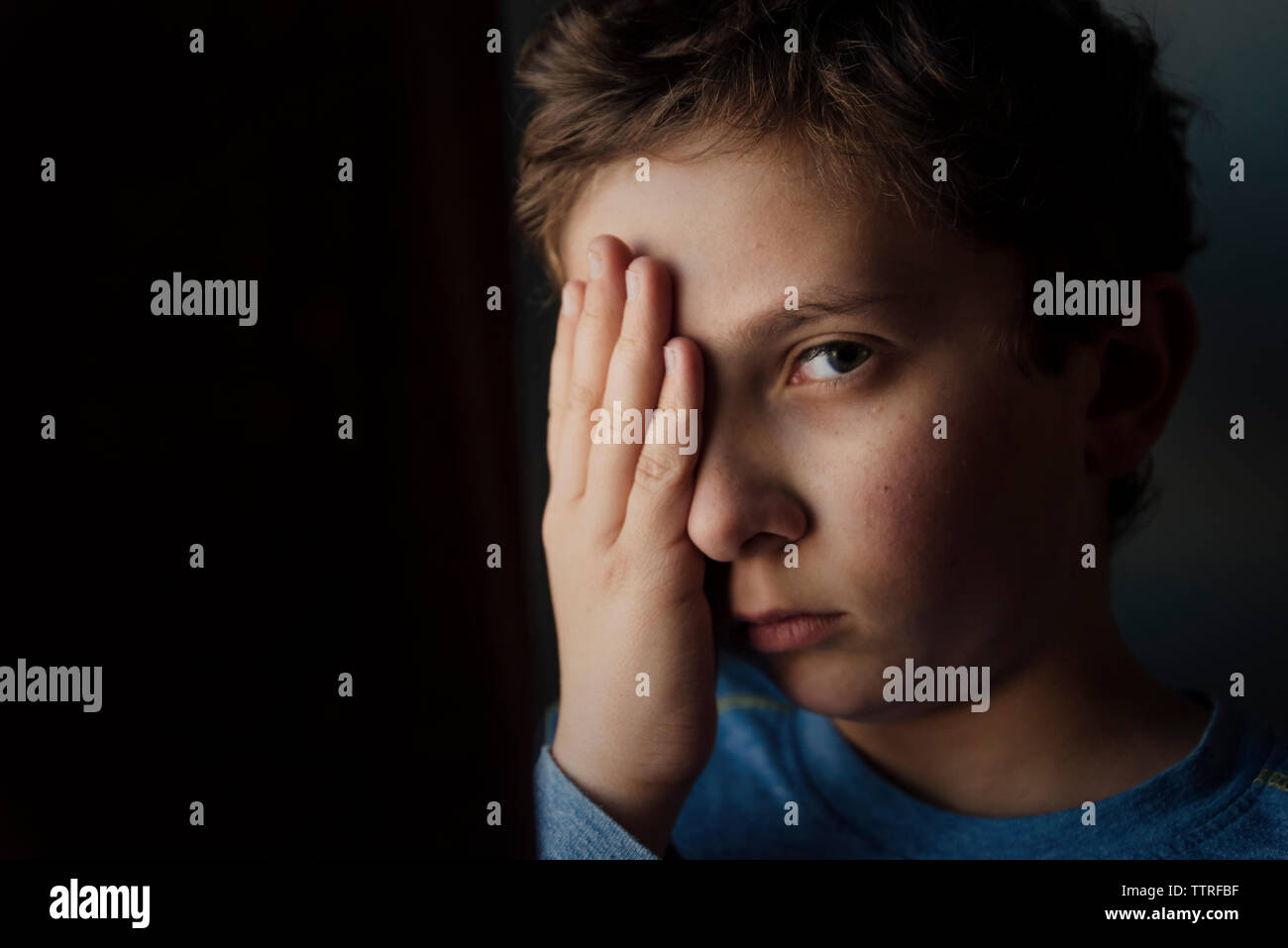 Close-up ritratto di ragazzo con la mano sulla faccia in camera oscura a casa Foto Stock
