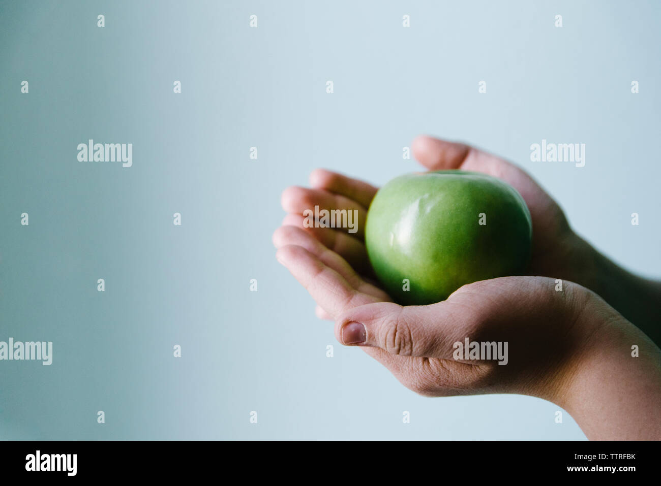 Mani tagliate di boy holding Granny Smith Apple contro la parete a casa Foto Stock