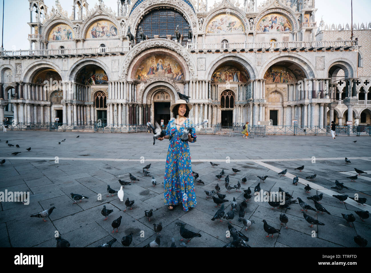 Lunghezza completa di turista in piedi in mezzo a uccelli di palissonatura sul sentiero contro la Basilica di San Marco Foto Stock