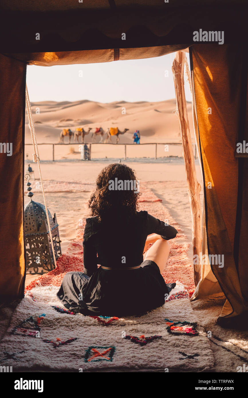 Vista posteriore della donna seduta su una coperta al deserto del Sahara visto attraverso la tenda Foto Stock