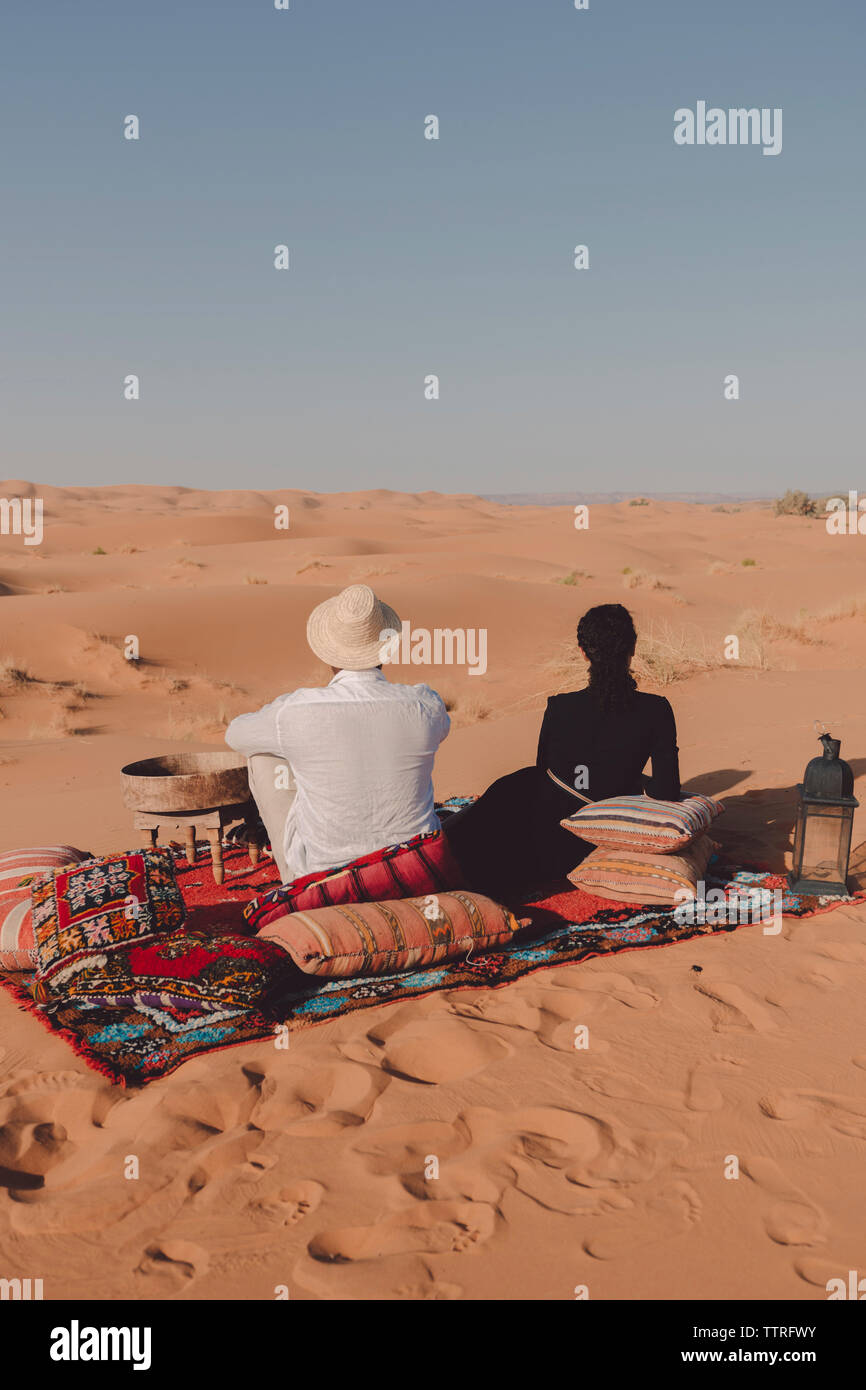 Vista posteriore di amici seduti su una coperta al deserto del Sahara contro il cielo chiaro durante la giornata di sole Foto Stock
