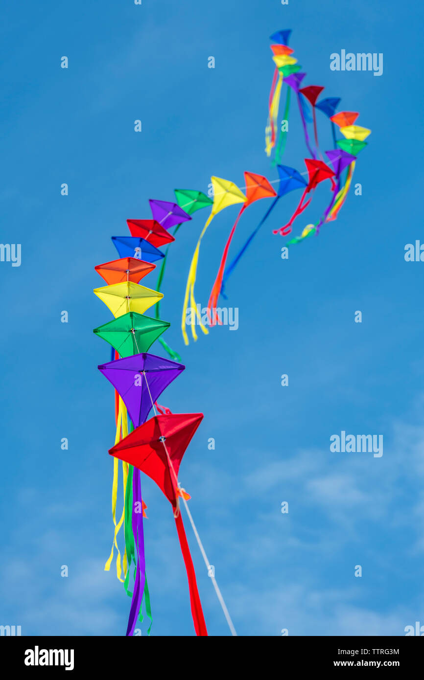 Una fila di aquiloni colorati su una singola linea contro un cielo blu chiaro. Foto Stock