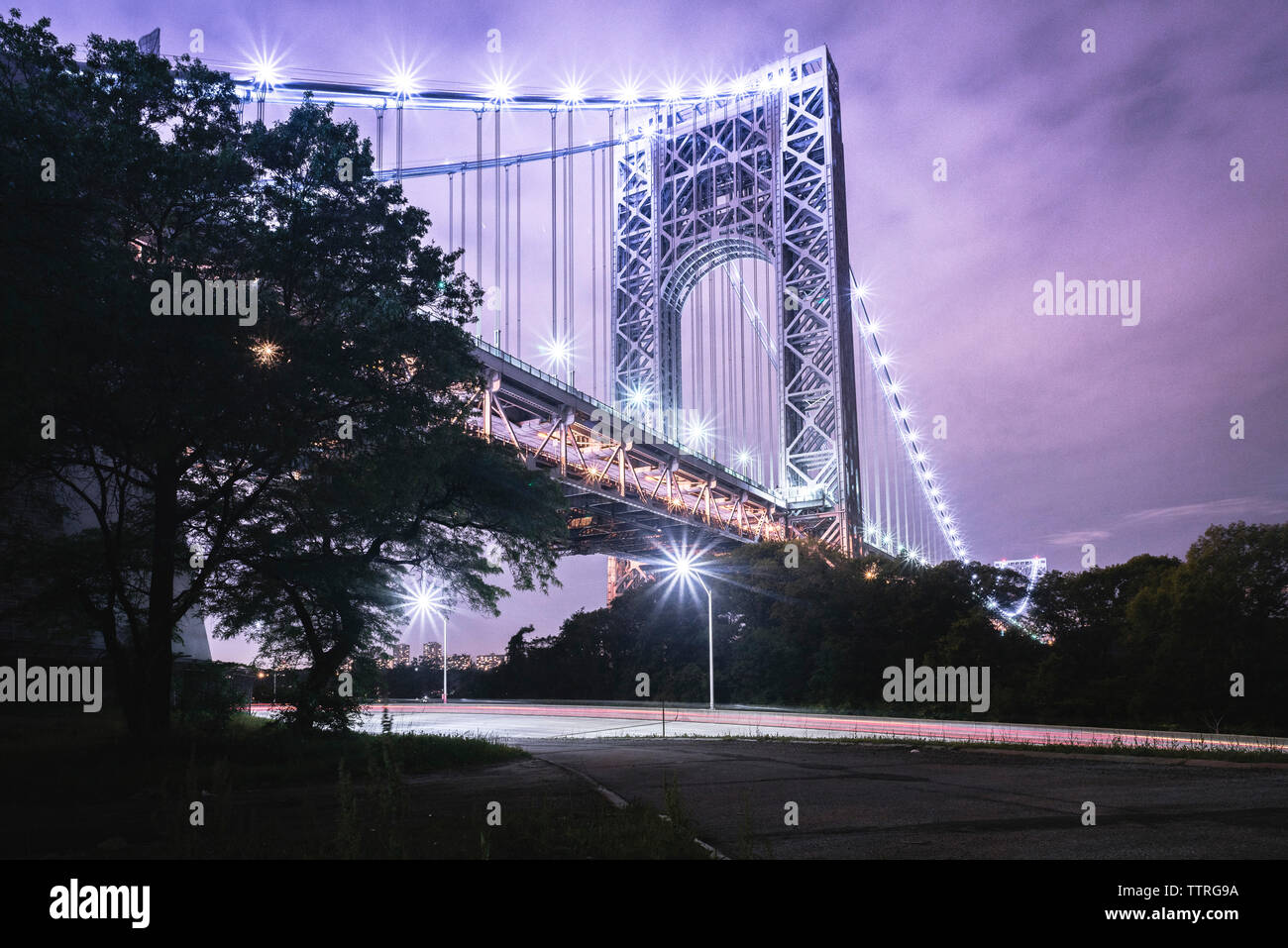 Basso angolo di vista illuminata George Washington Bridge su sentieri di luce sulla strada contro il cielo al tramonto Foto Stock