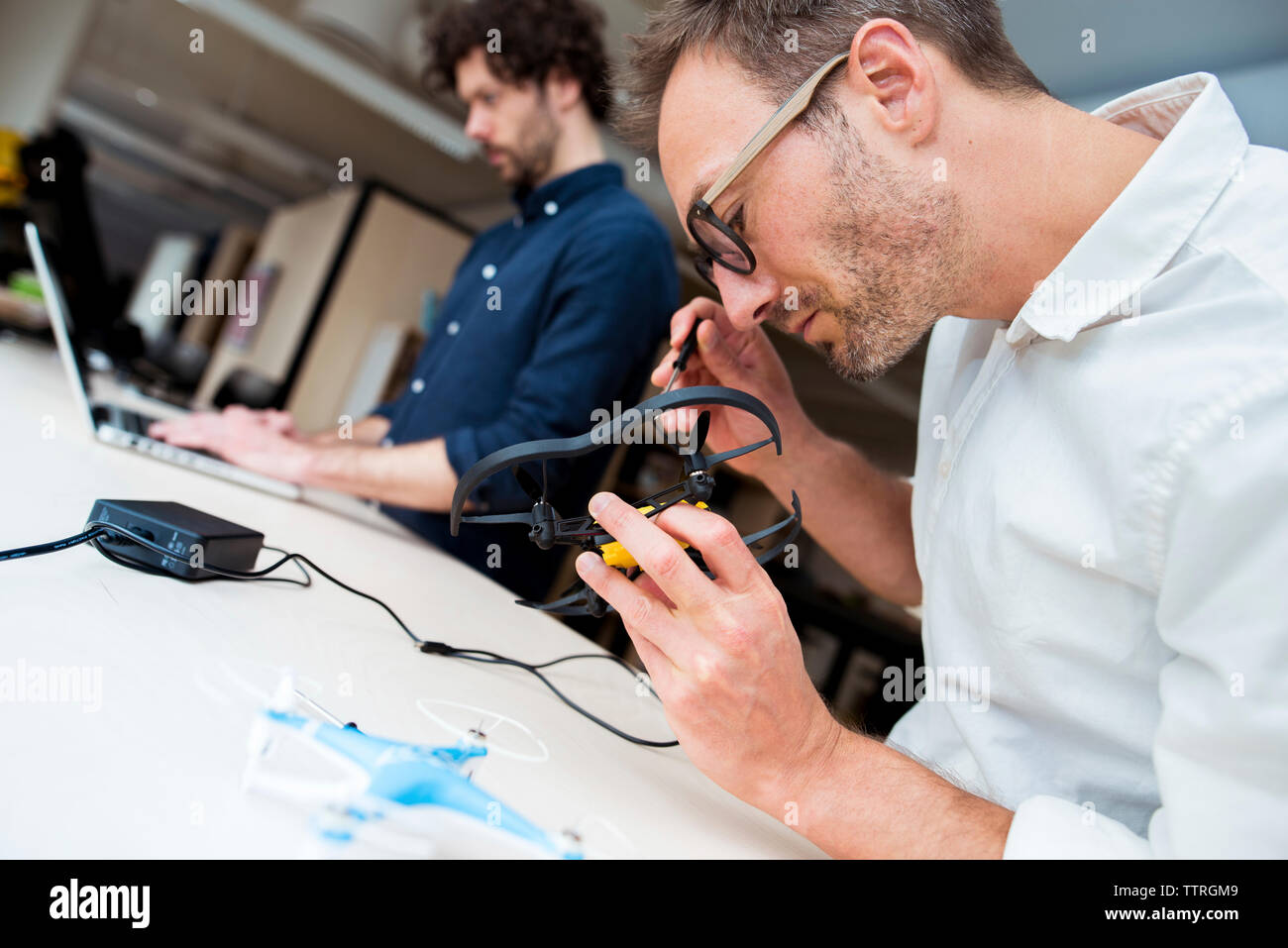 Ingegnere esaminando drone mentre un collega utilizzando il computer portatile in ufficio Foto Stock