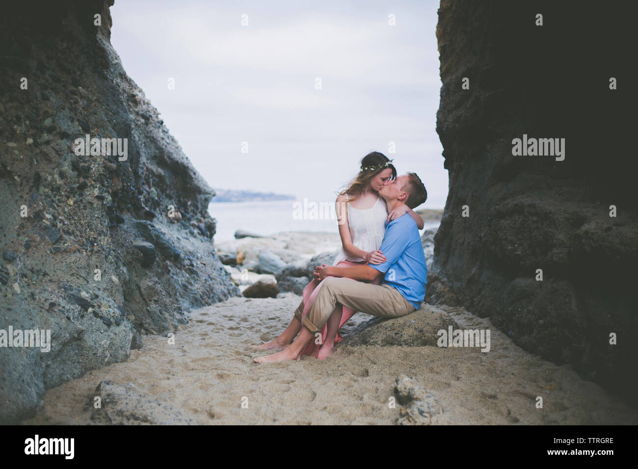 Coppia romantica baciare mentre è seduto sulla roccia alla spiaggia Foto Stock