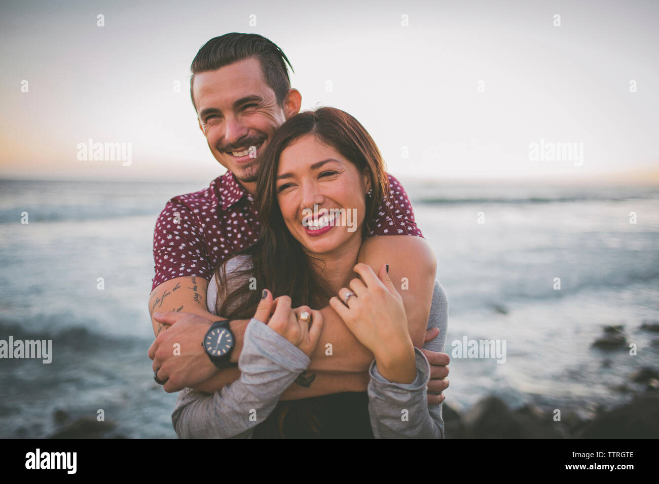 Felice coppia permanente al beach contro sky durante il tramonto Foto Stock