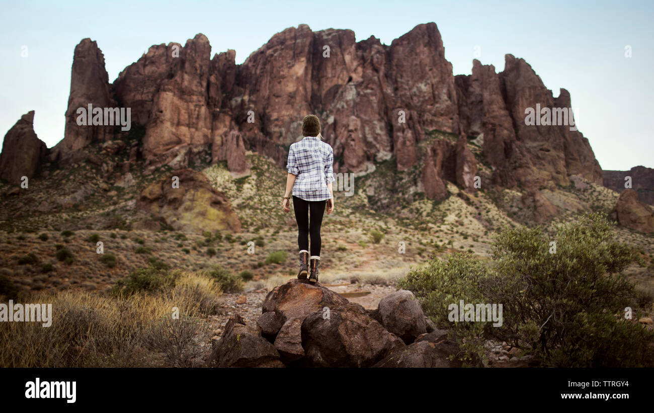 Vista posteriore di un'adolescente in piedi sulla parte superiore delle rocce contro la montagna Foto Stock