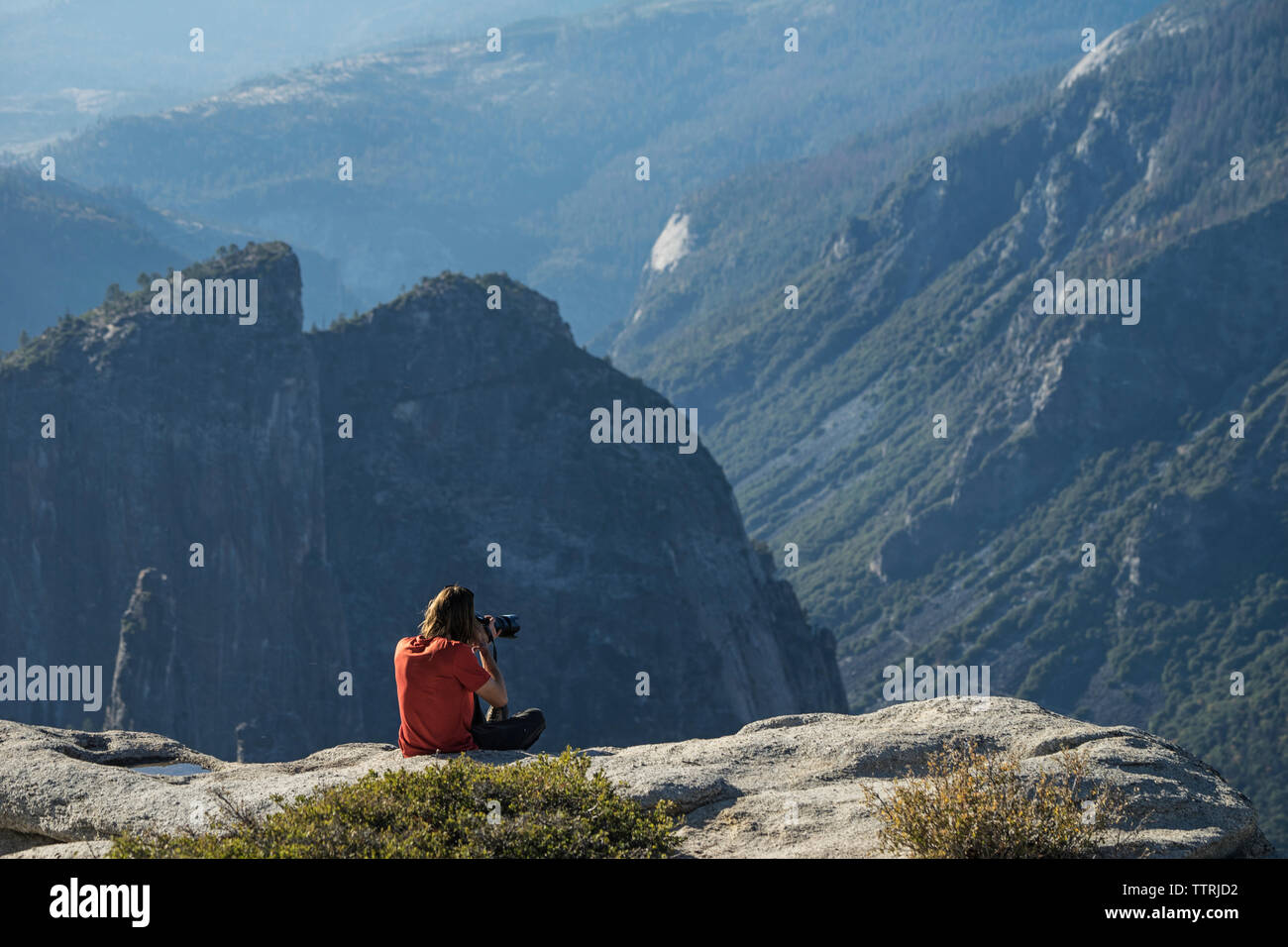 Uomo di fotografare mentre è seduto sulla scogliera al Parco Nazionale di Yosemite Foto Stock