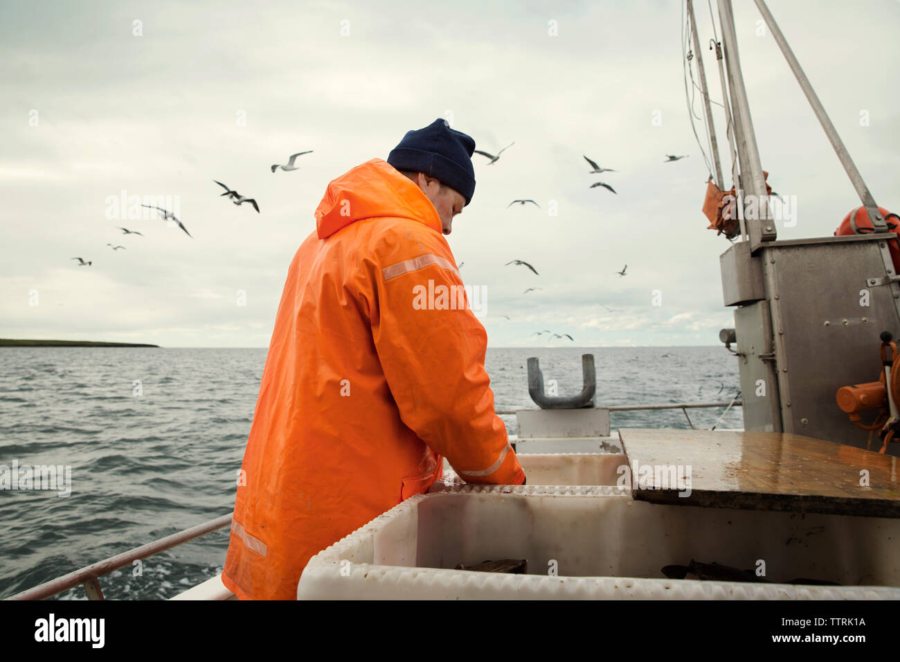 Pescatore in arancione indumenti da lavoro protettiva mentre si lavora in barca sul mare Foto Stock