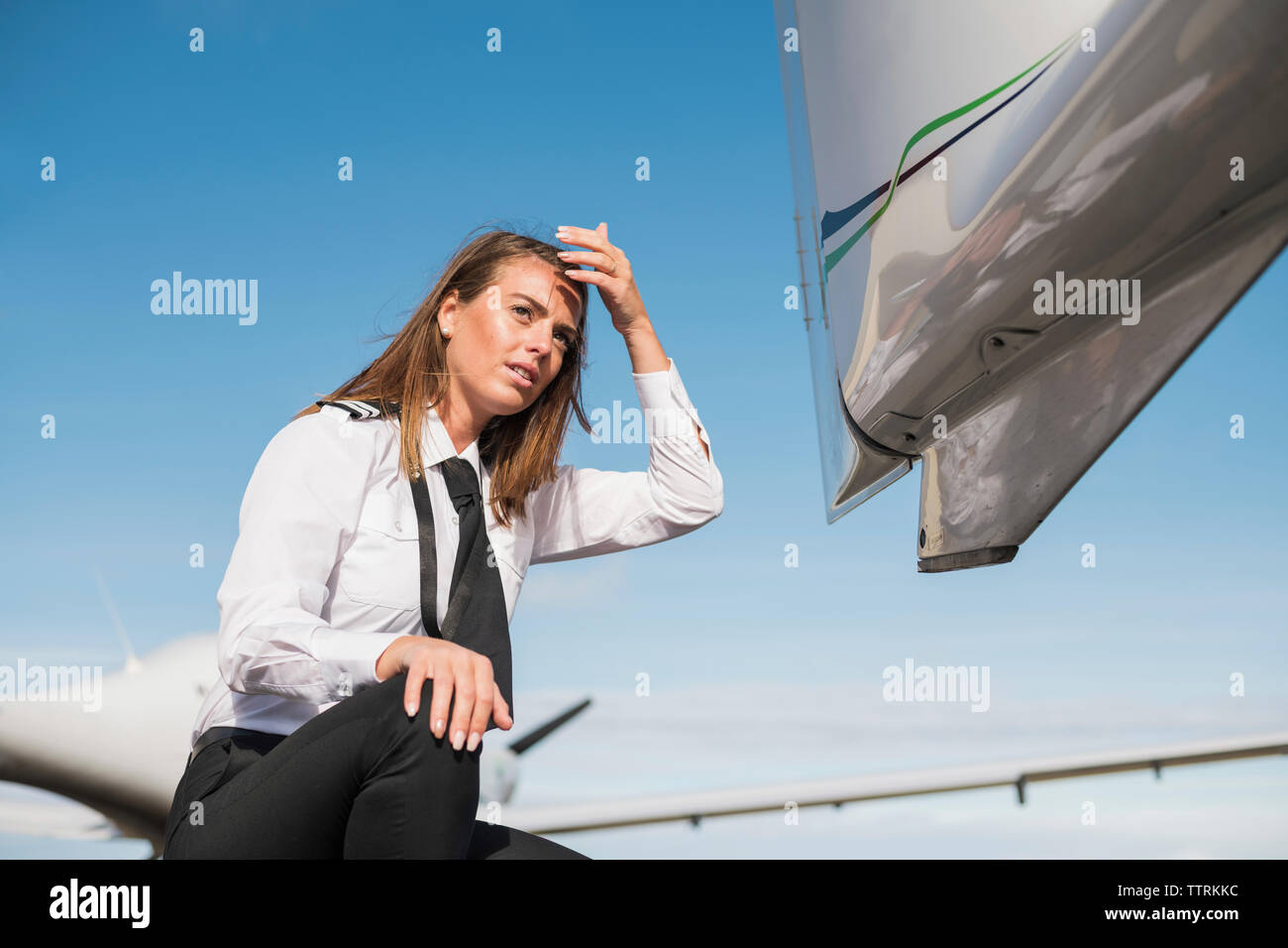 Basso angolo di vista tecnico femminile che guarda lontano mentre accovacciato in aereo contro il cielo blu durante la giornata di sole Foto Stock