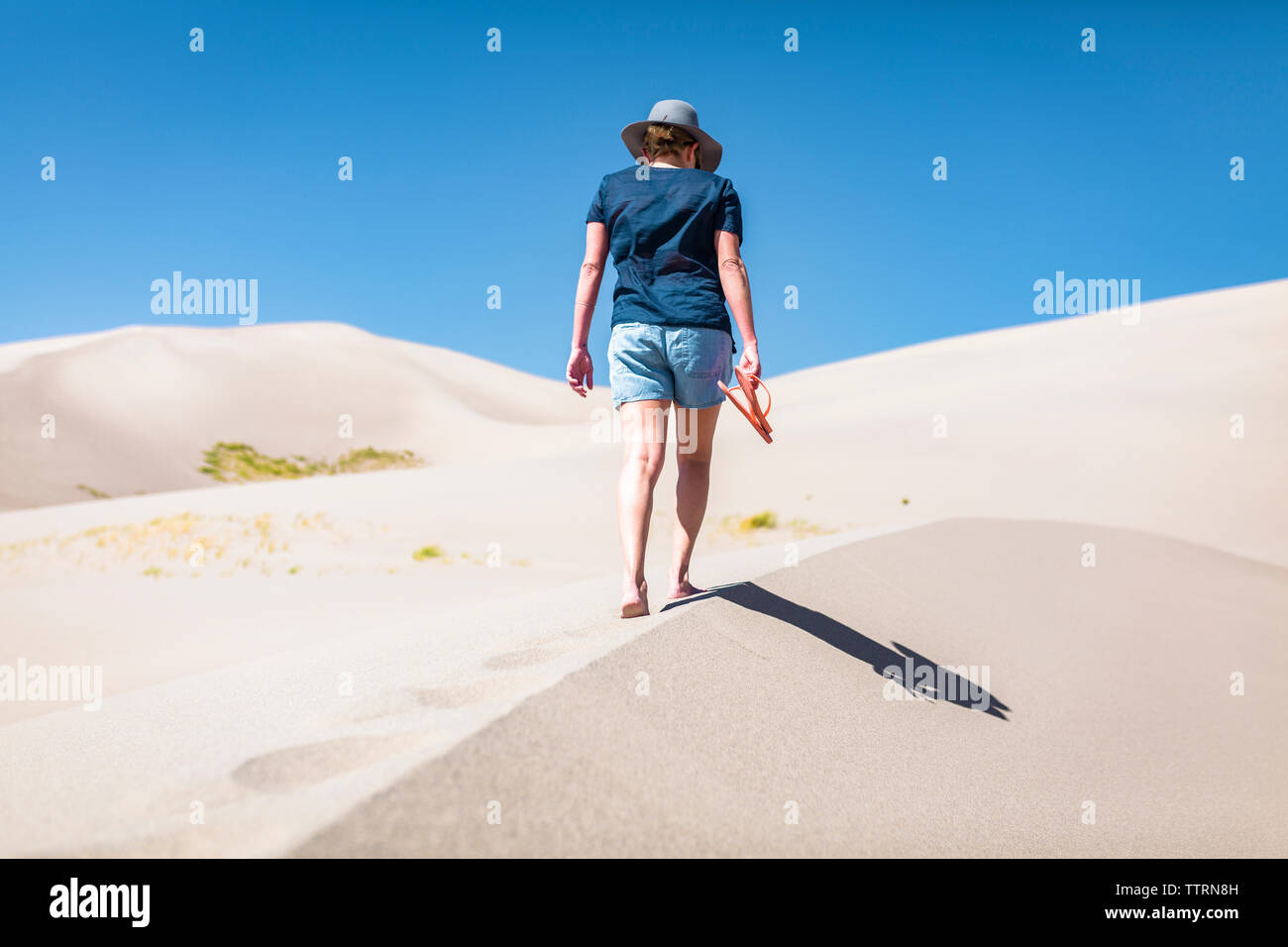 Vista posteriore della donna azienda flip-flop mentre passeggiate sulla sabbia a grandi dune di sabbia del Parco Nazionale durante la giornata di sole Foto Stock