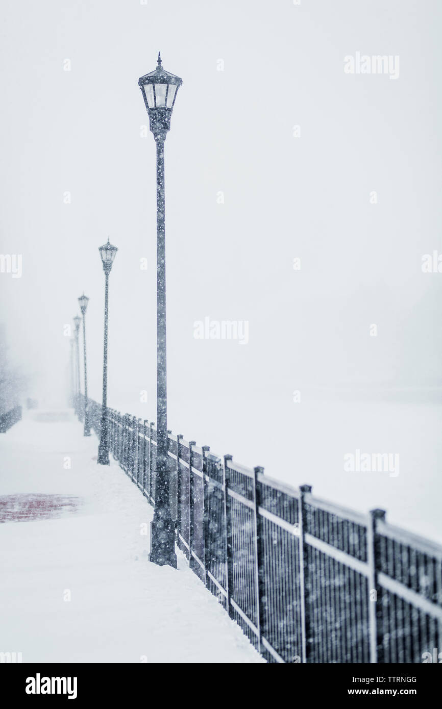 Le luci di strada dalla ringhiera metallica durante la nevicata Foto Stock