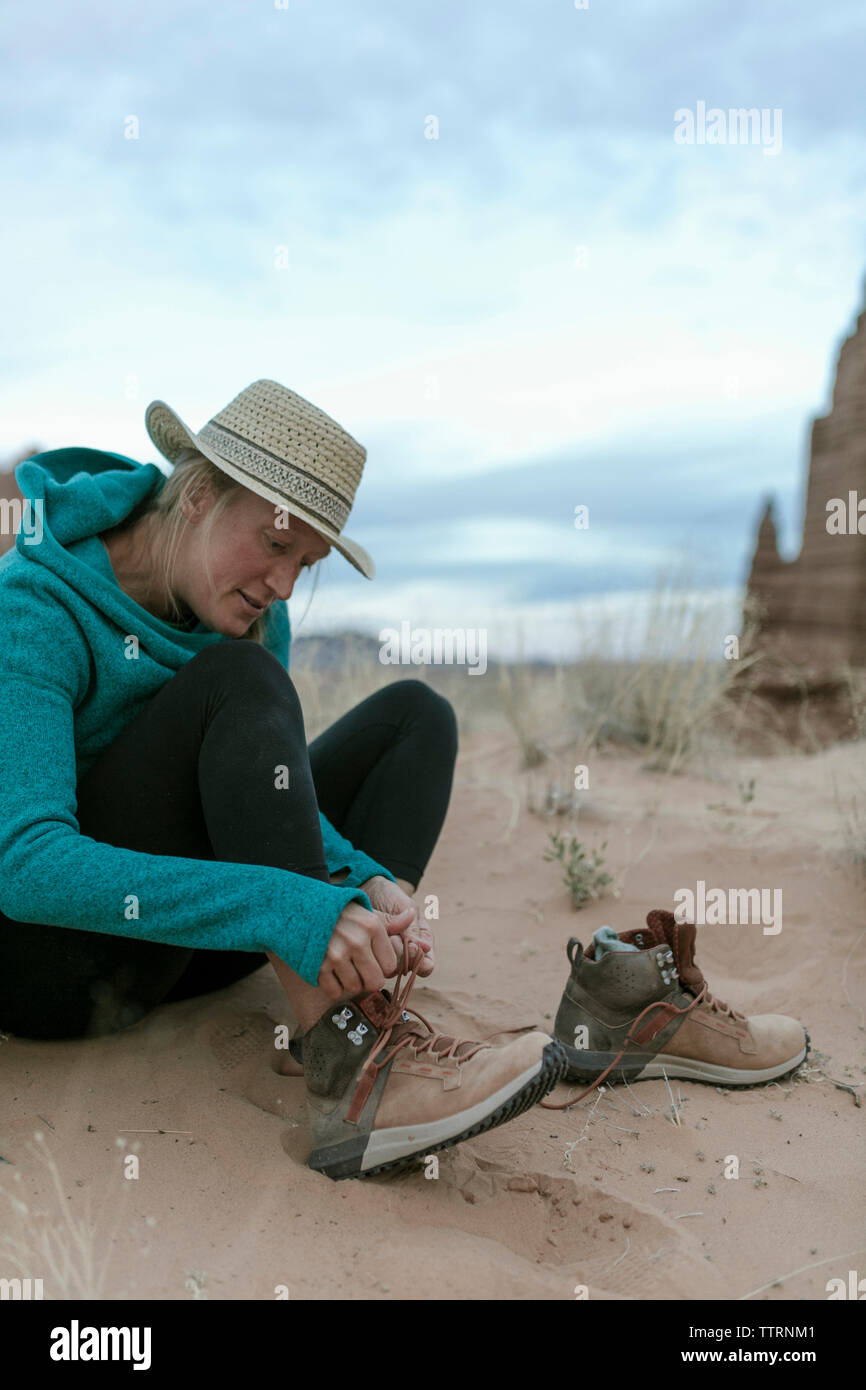 Escursionista femmina legatura di lacci delle scarpe mentre è seduto presso il desert Foto Stock