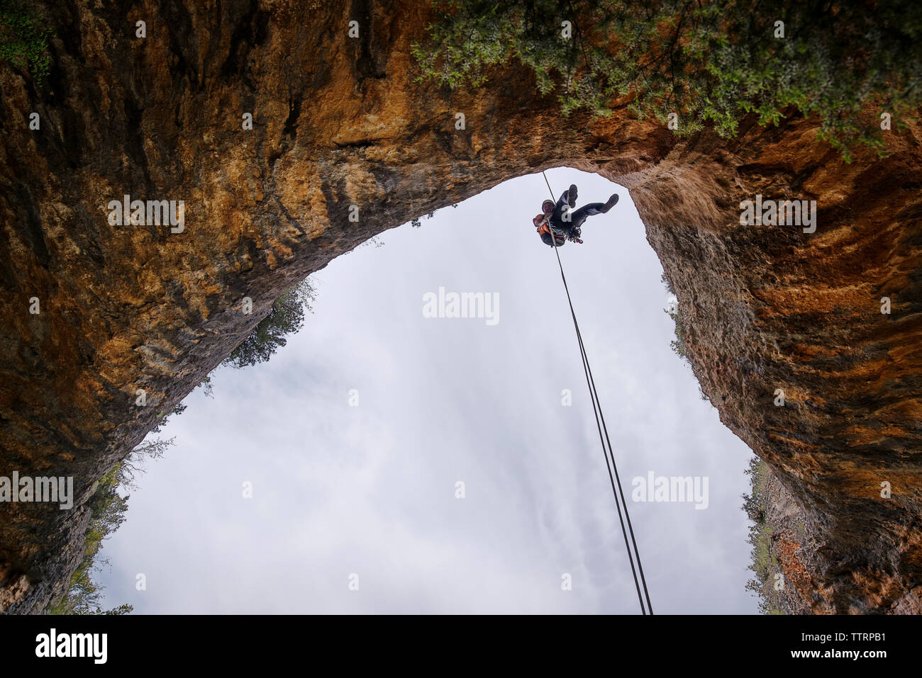 Basso angolo di visione dell'uomo rappelling da montagna Foto Stock