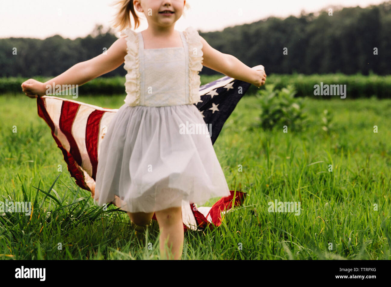 Sezione mediana della ragazza con bandiera americana mentre si cammina sul campo erboso Foto Stock