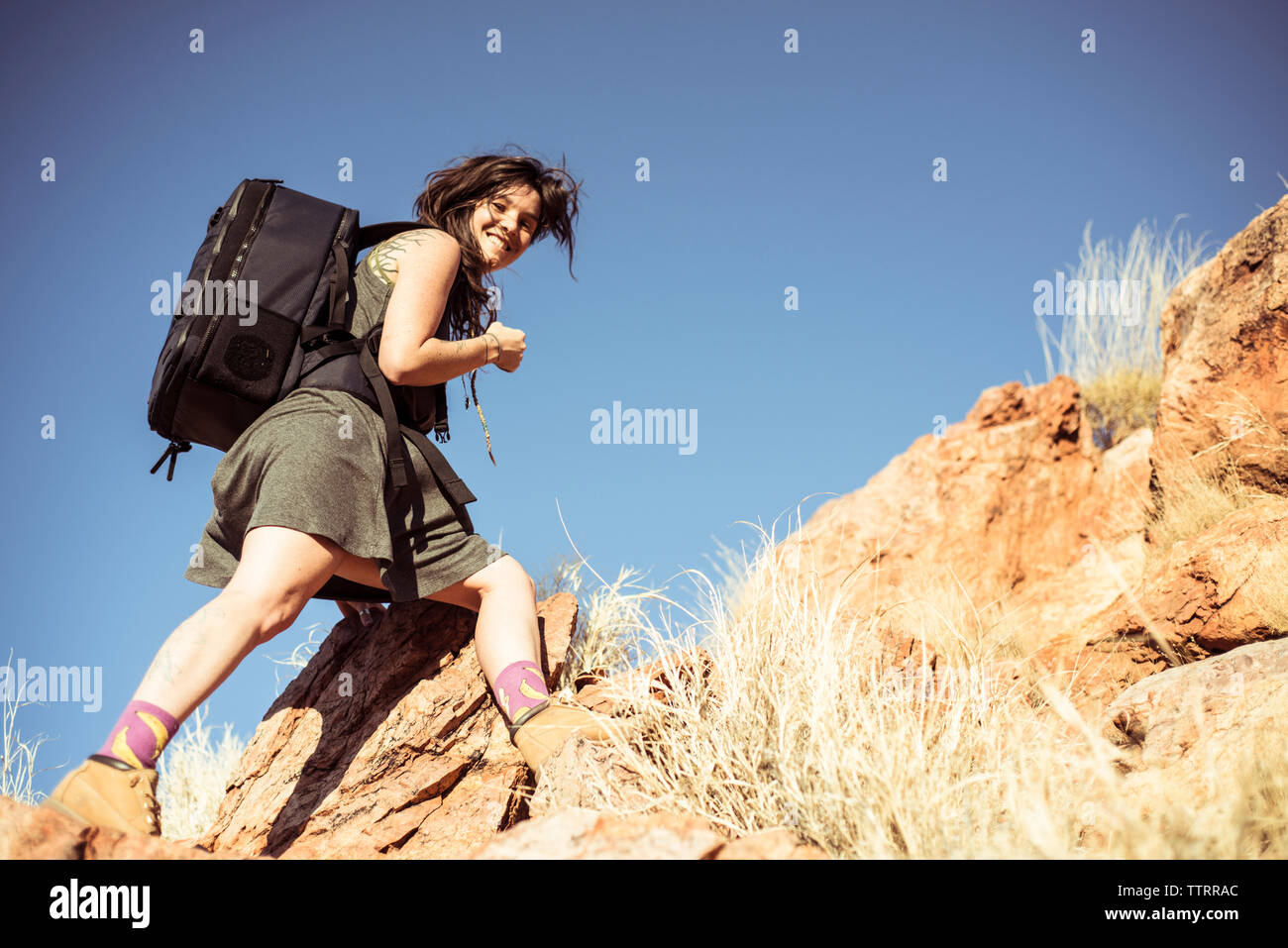 Angolo basso ritratto di donna con zaino montagna arrampicata contro il cielo chiaro durante la giornata di sole Foto Stock