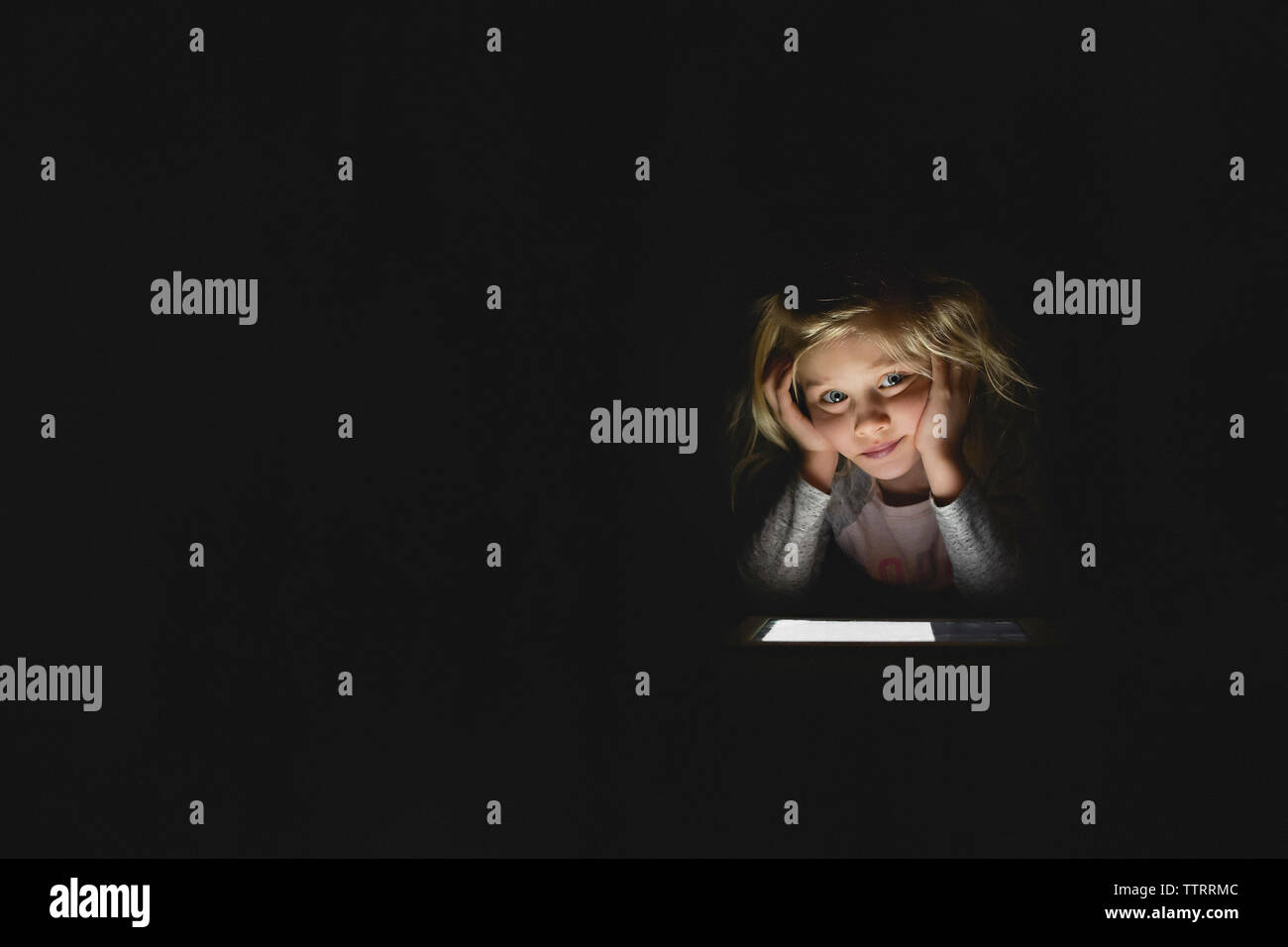 Annoiato ragazza utilizzando digitale compressa mentre è seduto in camera oscura a casa Foto Stock