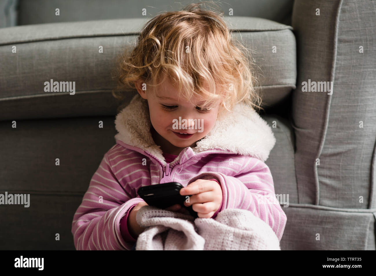 Ragazza utilizzando il cellulare mentre seduti in poltrona a casa Foto Stock