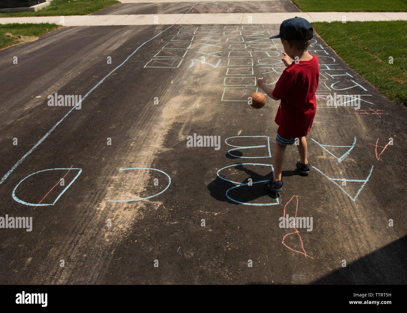 Vista posteriore del ragazzo giocando con la palla mentre permanente sulla strada con chalk disegno Foto Stock