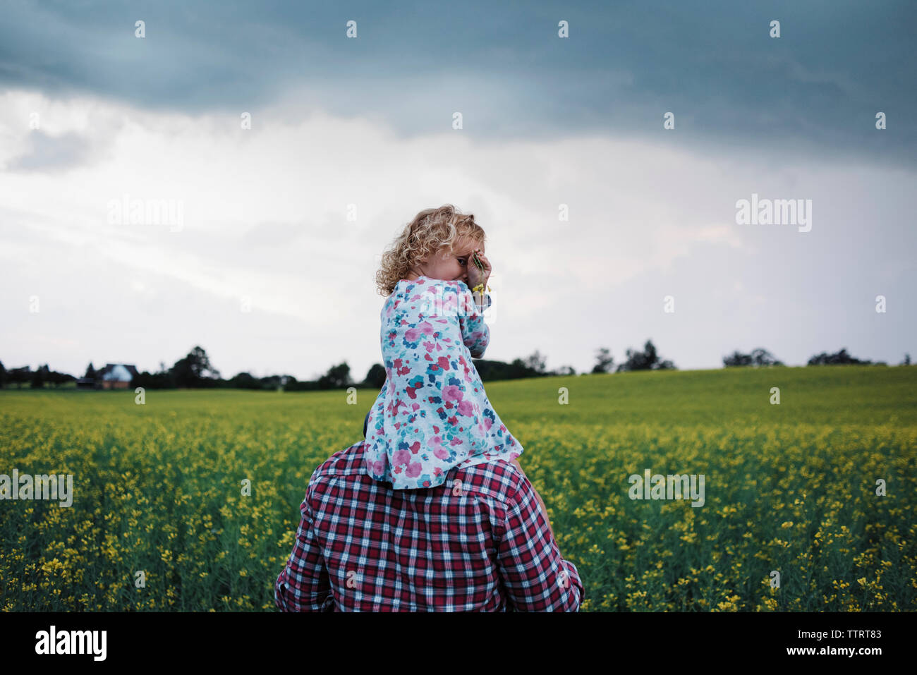 Ritratto della figlia essendo portati dal padre sulle spalle in campo contro nuvole temporalesche Foto Stock