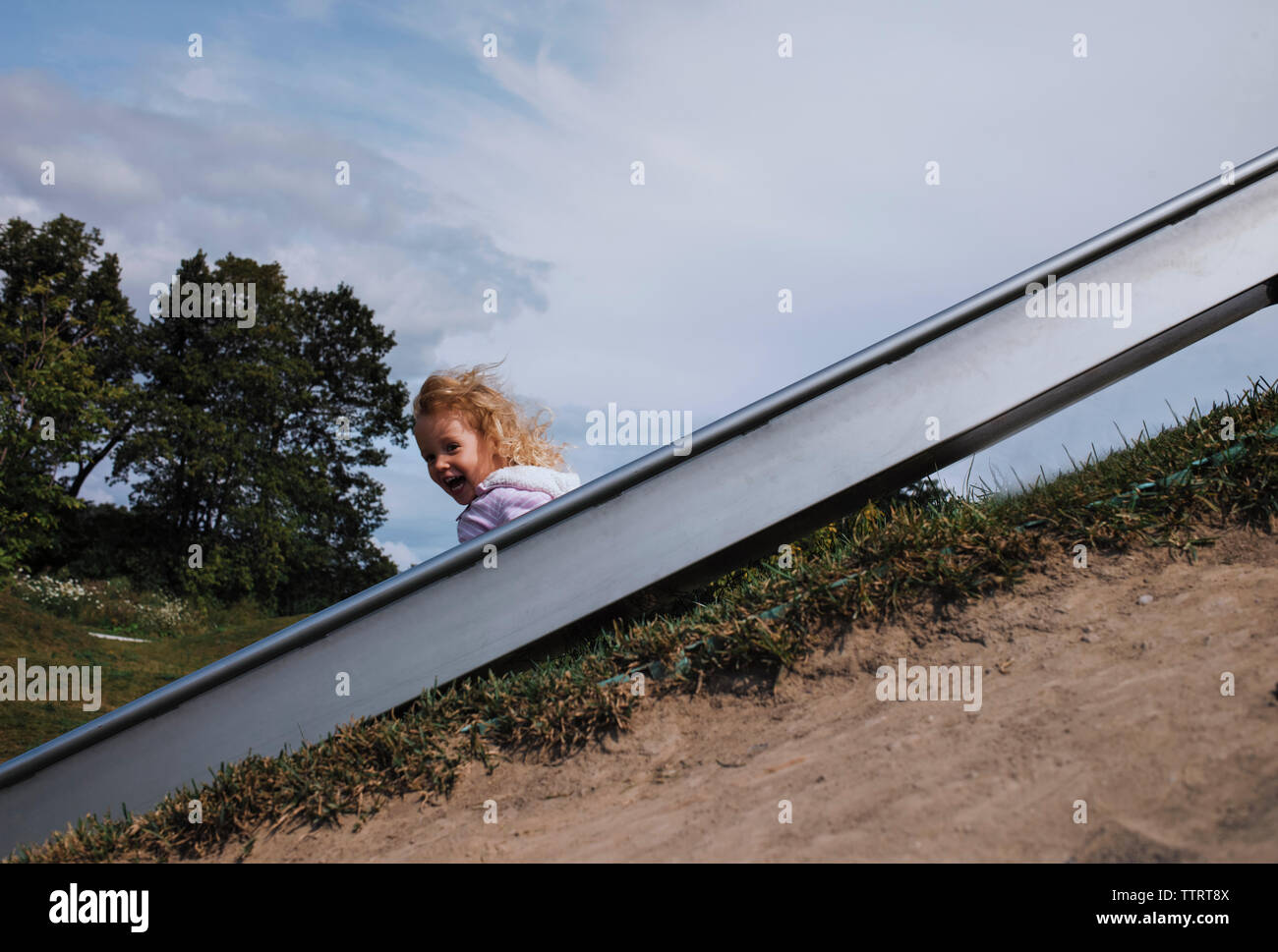 Ragazza che gioca sulla slitta a park contro sky Foto Stock