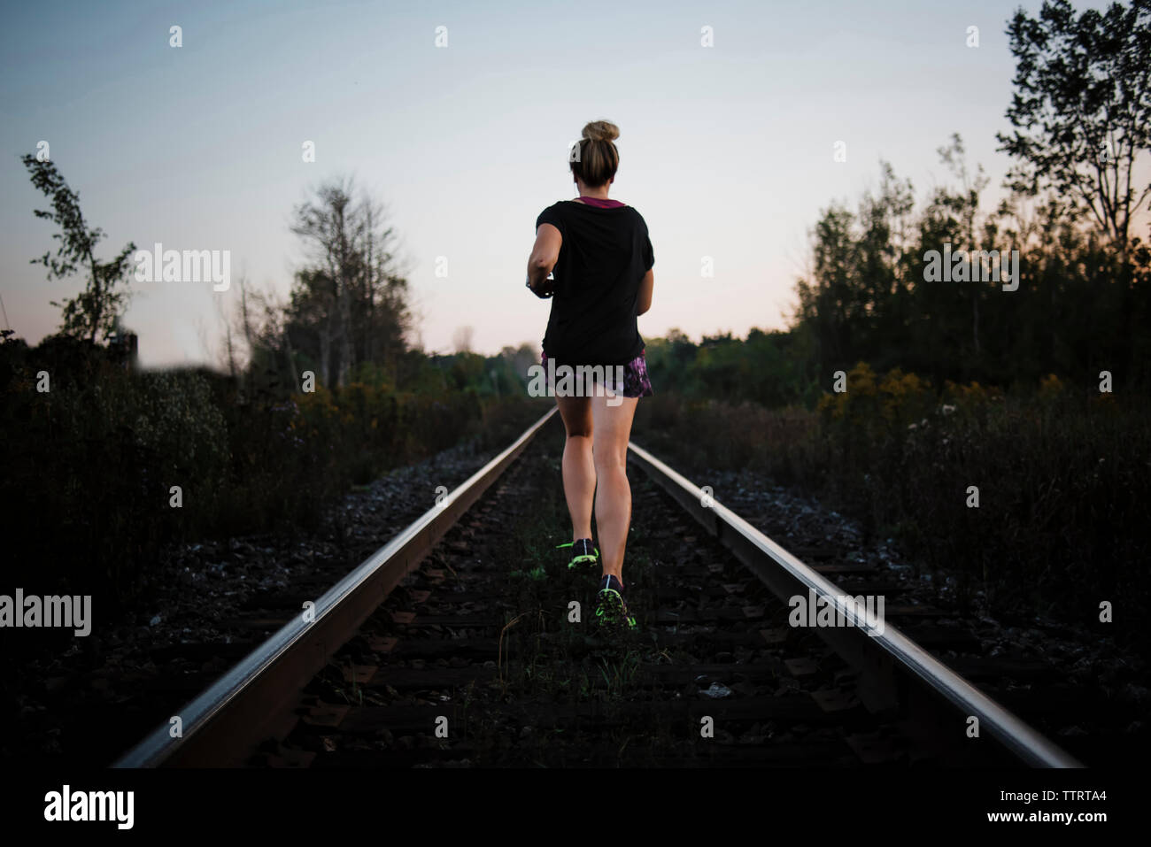 Vista posteriore della donna jogging sulla ferrovia via contro il cielo durante il tramonto Foto Stock