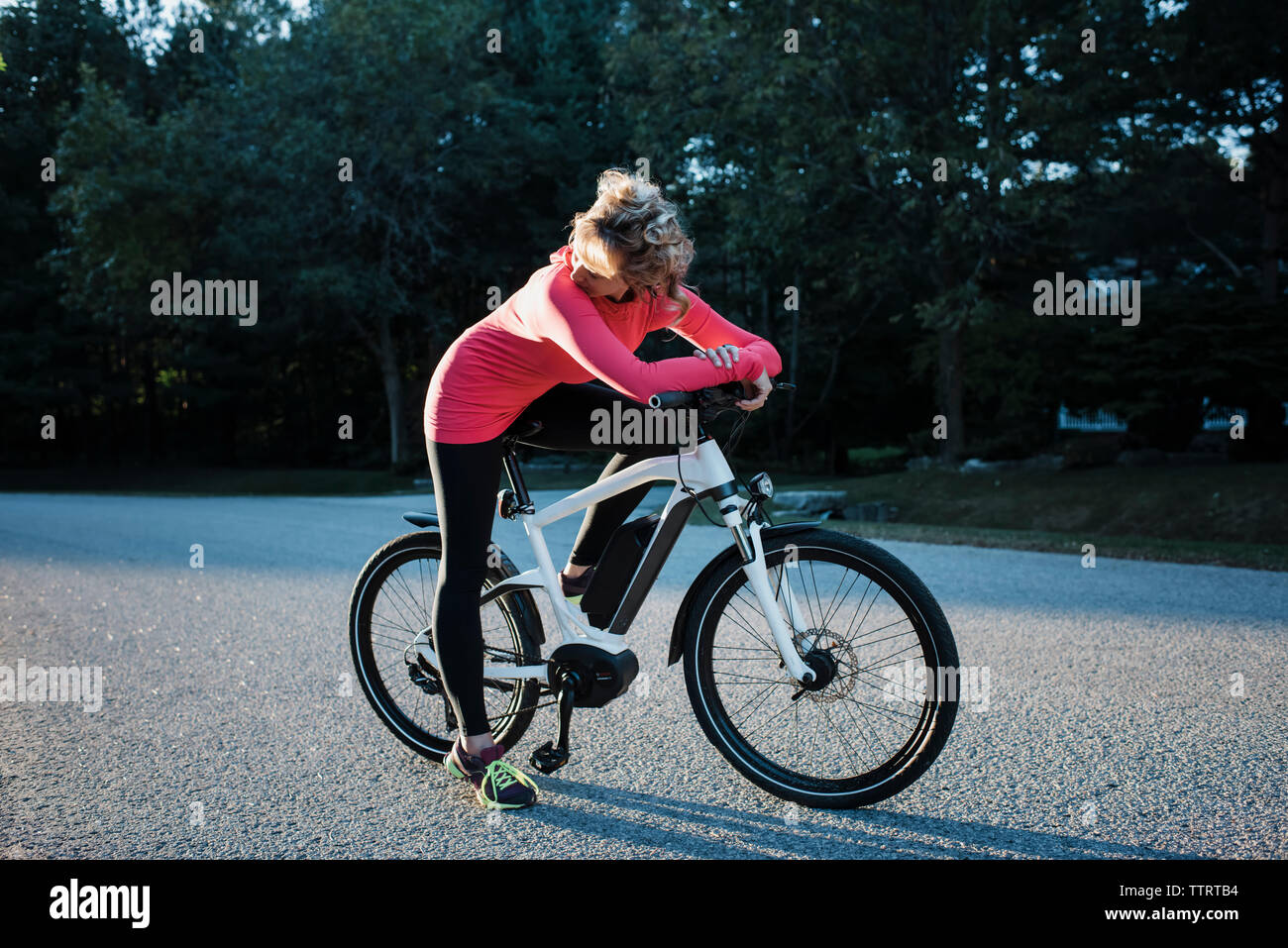 Donna che guarda lontano mentre è seduto in mountain bike al country road Foto Stock