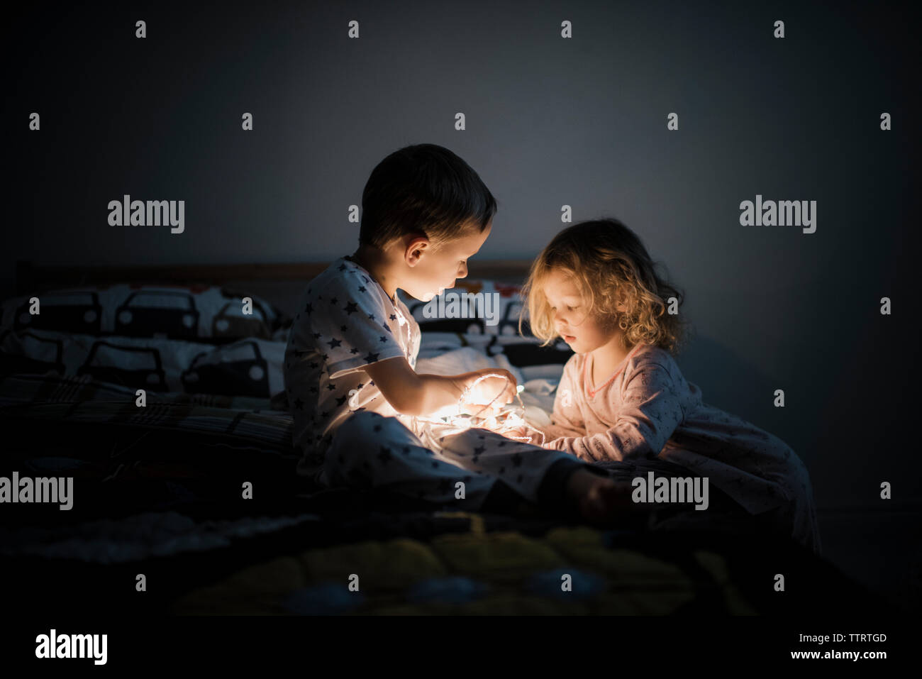 Fratelli illuminato con luci di stringa seduta sul letto di casa Foto Stock