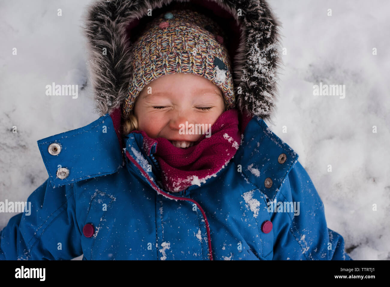 Angolo di Alta Vista della ragazza sorridente con gli occhi chiusi che giace sulla neve campo coperto Foto Stock