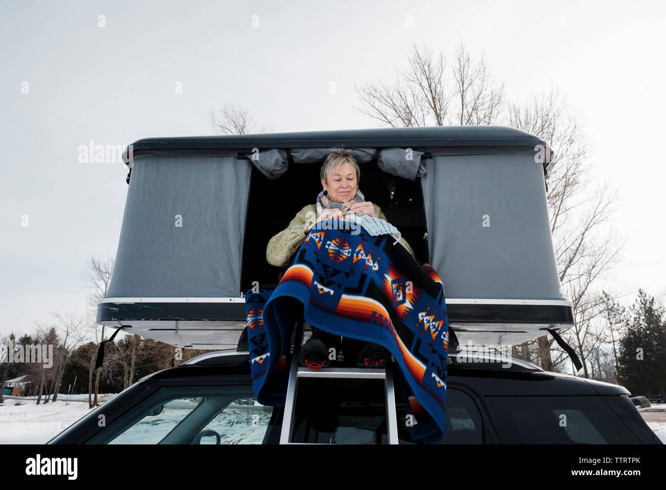 Basso angolo di visione della donna maglia mentre è seduto nella tenda del tetto sulla vettura durante il periodo invernale Foto Stock