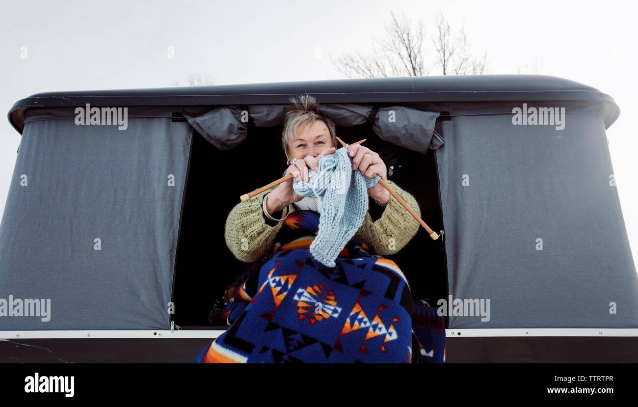 Angolo basso ritratto di donna maglia mentre è seduto nella tenda del tetto sulla vettura durante il periodo invernale Foto Stock