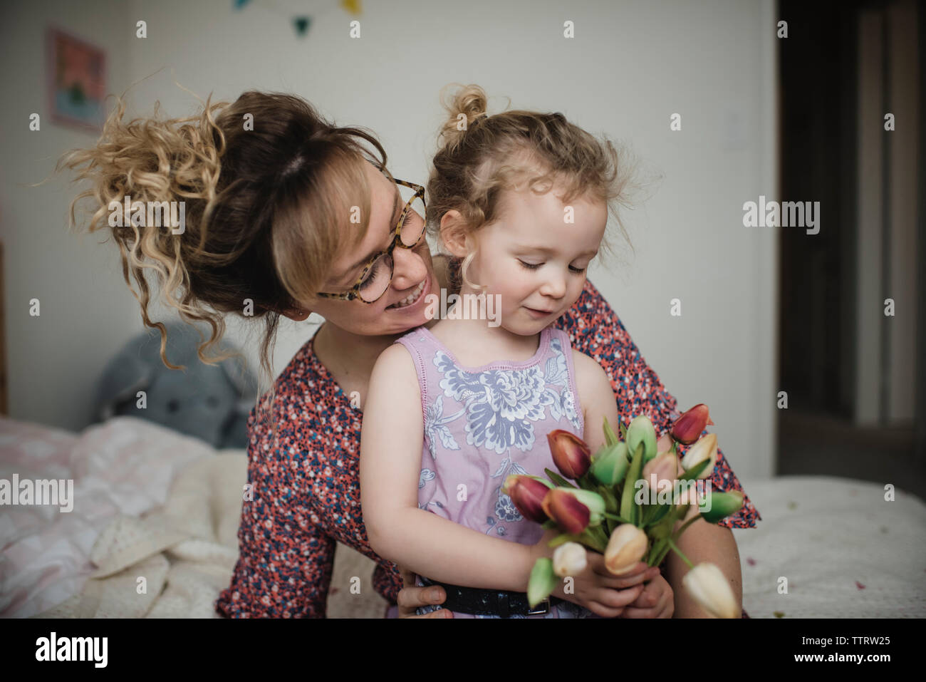 Figlia di tulipani di contenimento mentre è seduto con la madre sul letto di casa Foto Stock