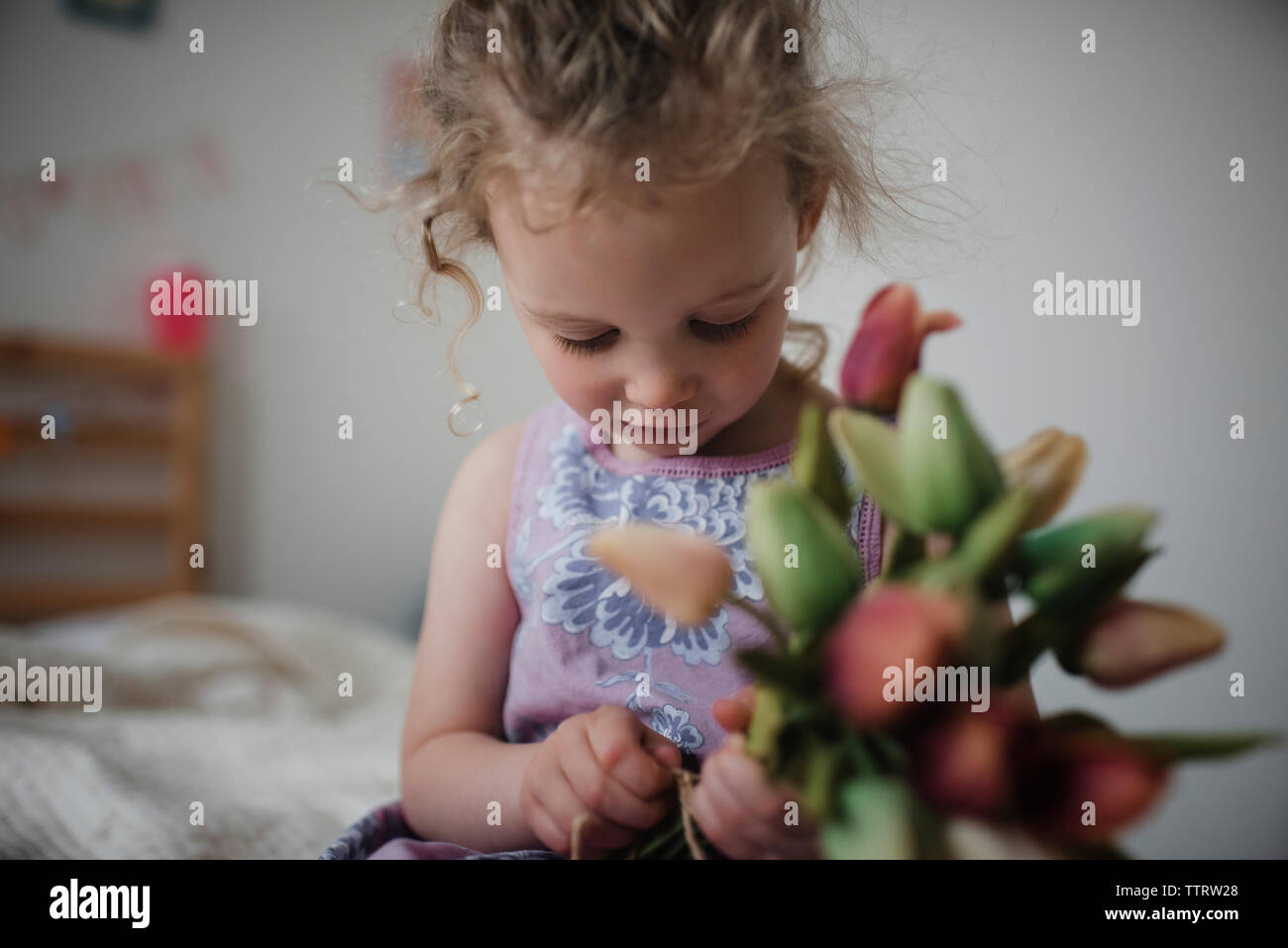 Close-up della ragazza con i tulipani durante la seduta sul letto di casa Foto Stock