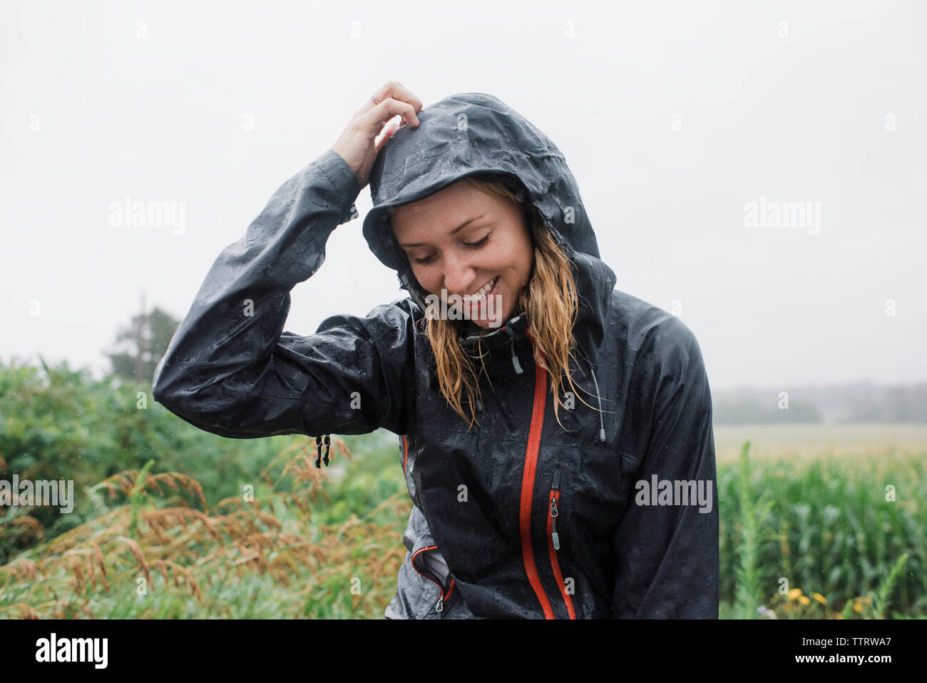 Donna felice in un impermeabile in piedi in mezzo a piante contro il cielo durante la stagione delle piogge Foto Stock