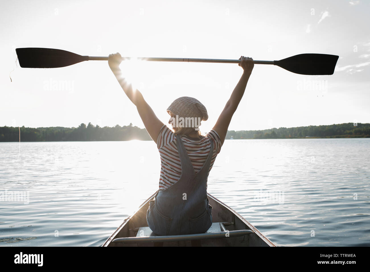 Vista posteriore della donna con le braccia sollevate holding oar seduti in barca sul lago a Algonquin Provincial Park Foto Stock