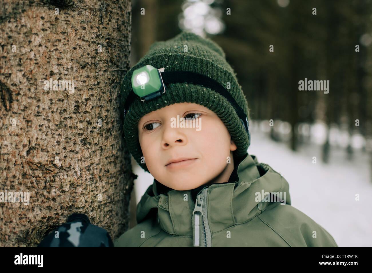Ragazzo giovane appoggiato su di un albero di pensare con la torcia da testa su in inverno Foto Stock