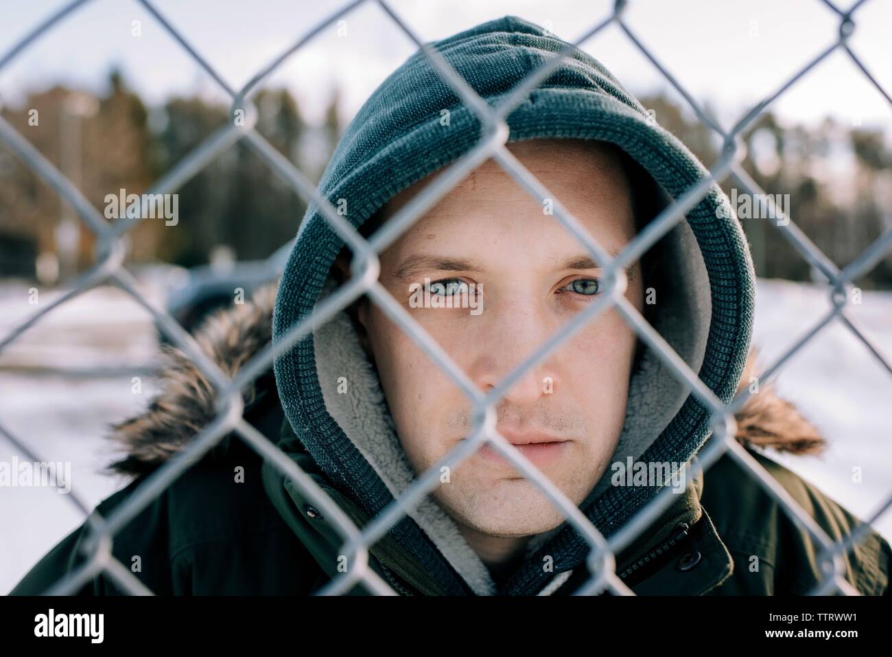 Ritratto di un uomo guardando attraverso un recinto di filo con la sua cappa su Foto Stock