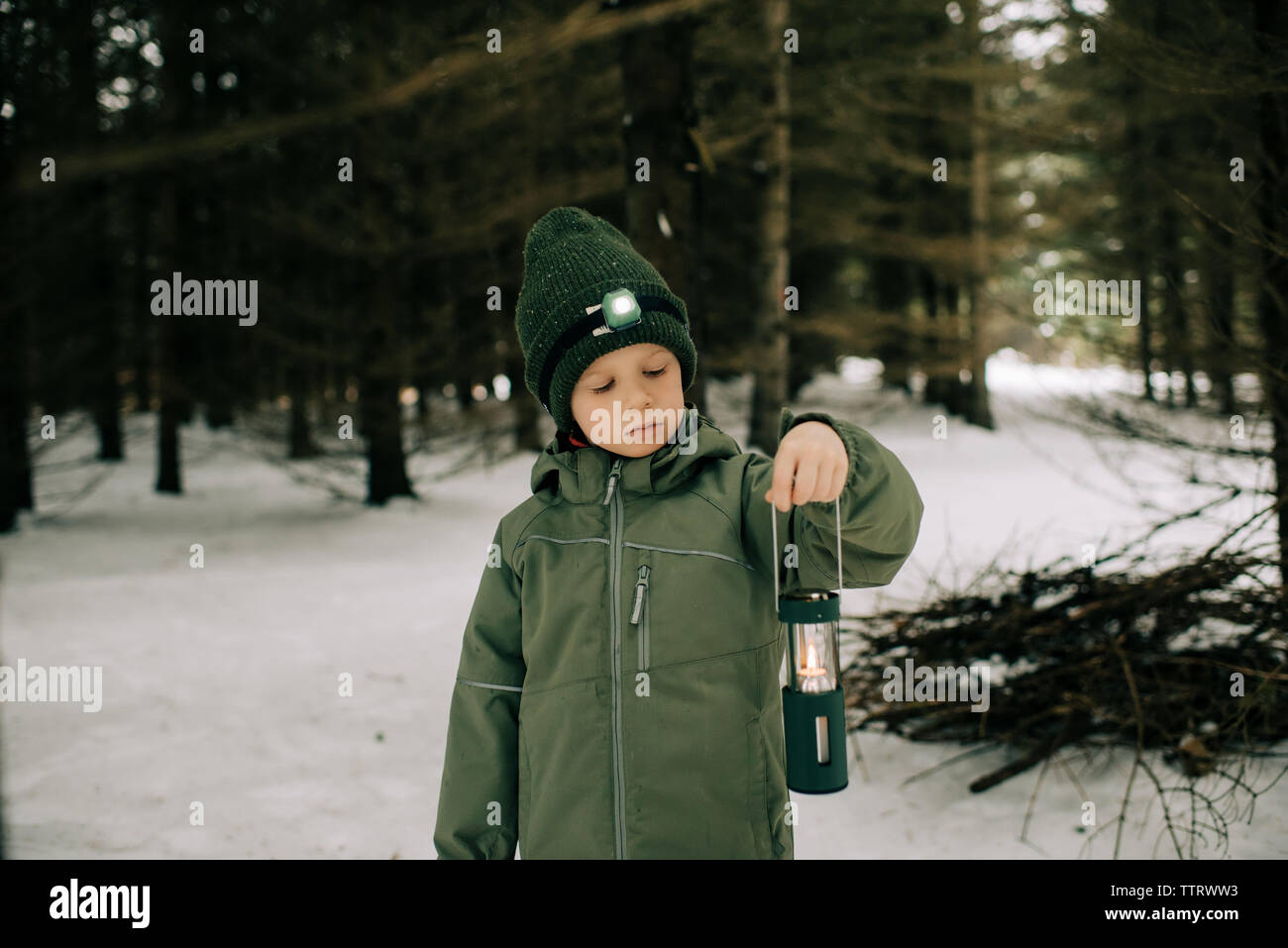 Ragazzo in piedi in una coperta di neve forest holding lanterna torcia e pensare Foto Stock