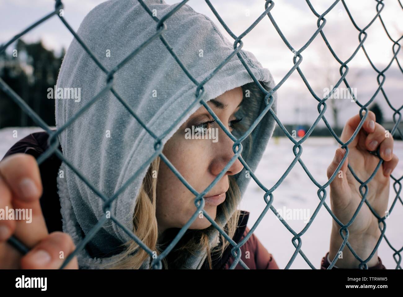 Ritratto di donna con il suo cappuccio di tenuta su di una recinzione metallica pensando Foto Stock