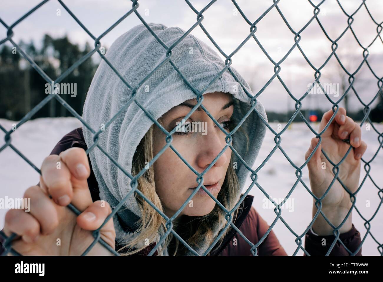 Ritratto di una donna in possesso di una recinzione metallica in inverno con cappa su Foto Stock