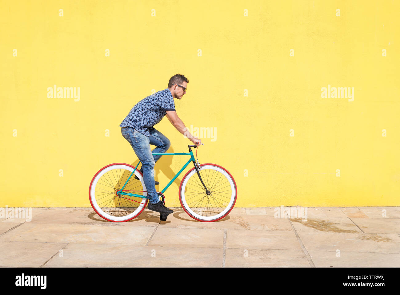 Vista laterale dell'uomo Bicicletta Equitazione contro la parete gialla al marciapiede in città Foto Stock