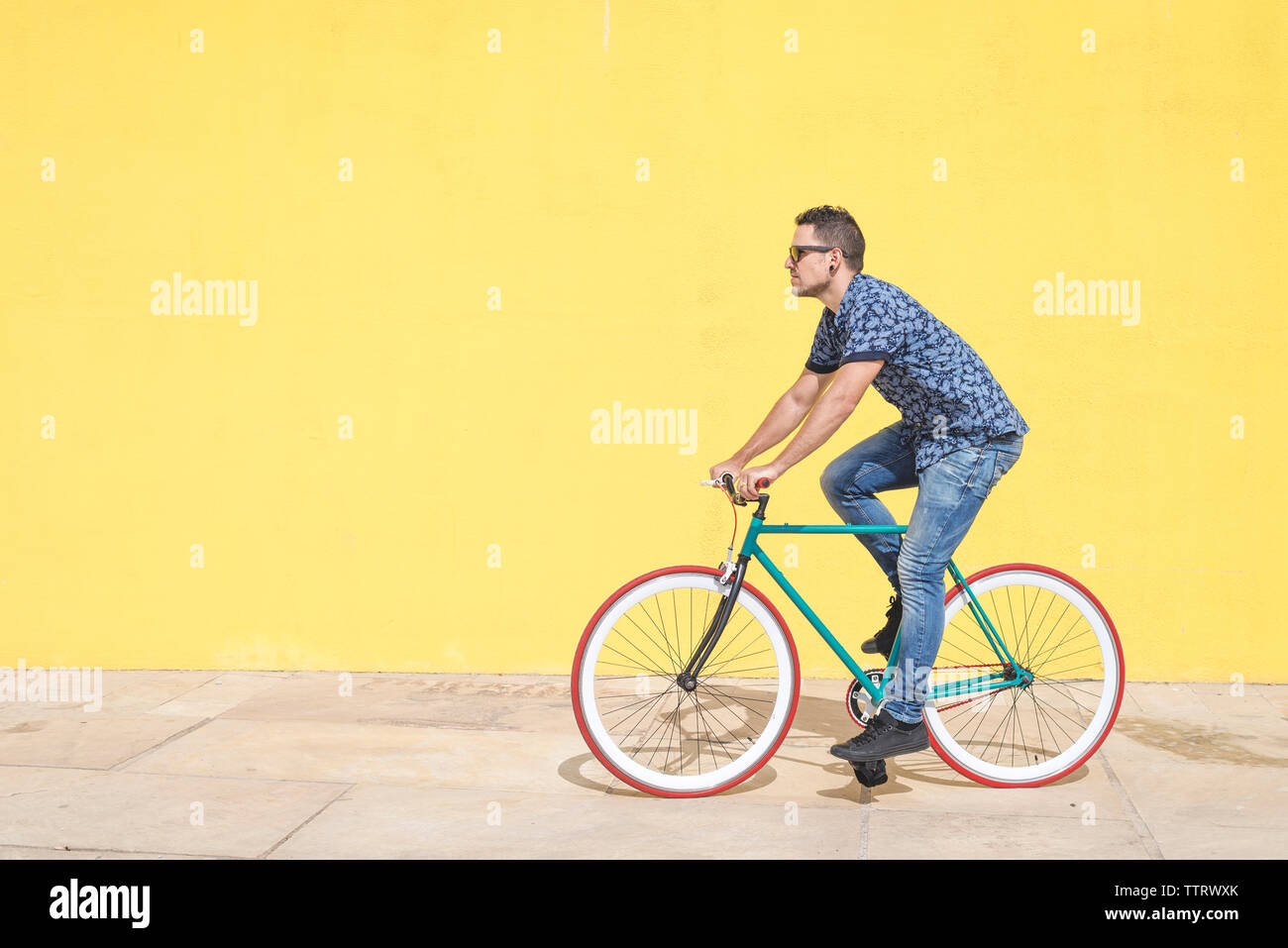 Lunghezza completa di uomo Bicicletta Equitazione contro la parete gialla al marciapiede in città Foto Stock