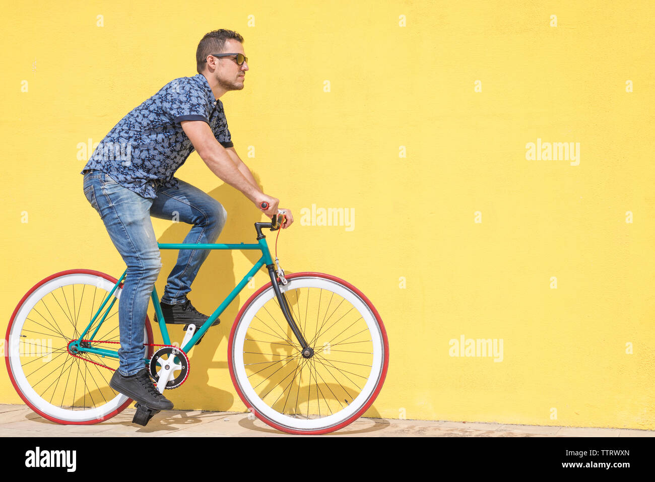 Uomo Bicicletta Equitazione contro la parete gialla al marciapiede in città Foto Stock