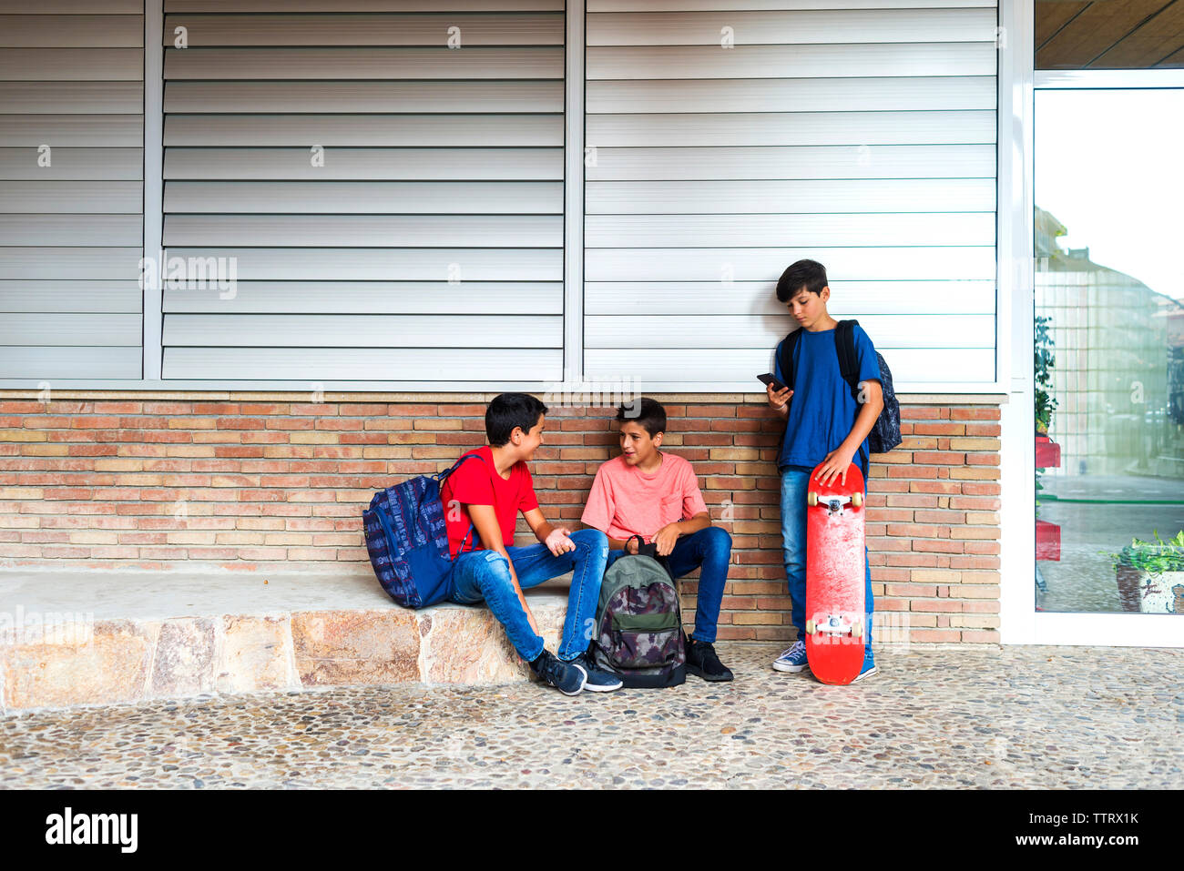 Boy utilizzando il cellulare mentre gli amici parlando da edificio scolastico Foto Stock