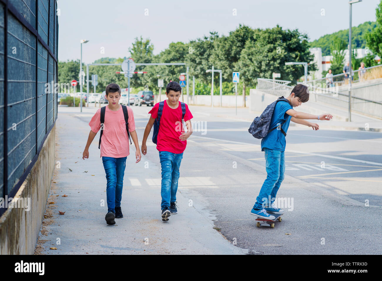 Amici a piedi il ragazzo con lo skateboard su strada Foto Stock